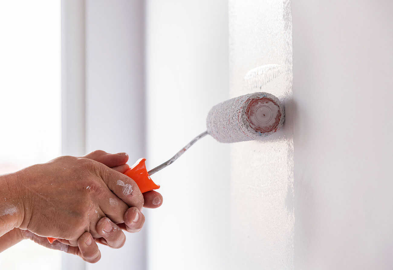 Person rolling white paint onto a wall.