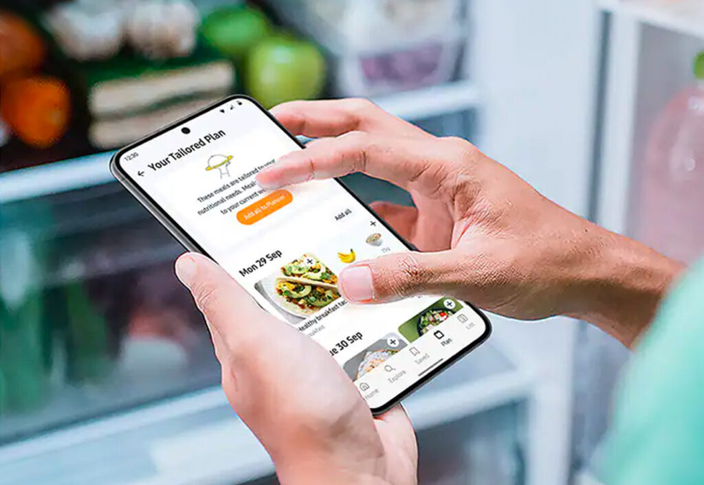 Person reading a meal planner off a phone in front of a fridge.