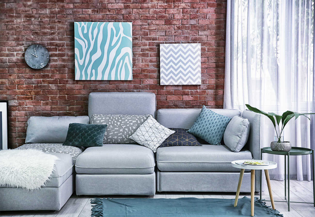 Sheer curtains next to a red-brick wall and grey leather sofa. 