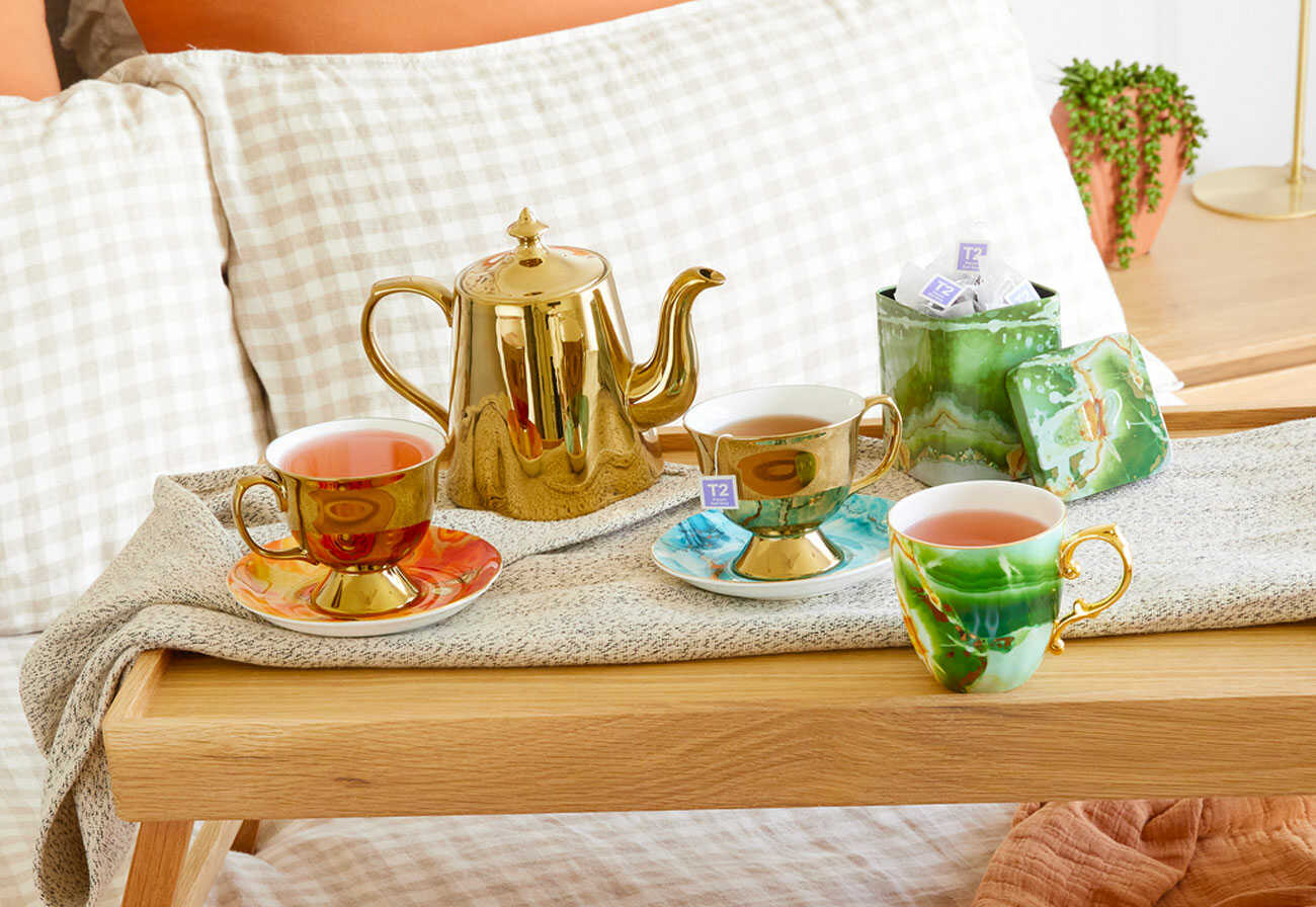 T2 Onyx Gold Teapot on a coffee table next to mugs of fresh tea.