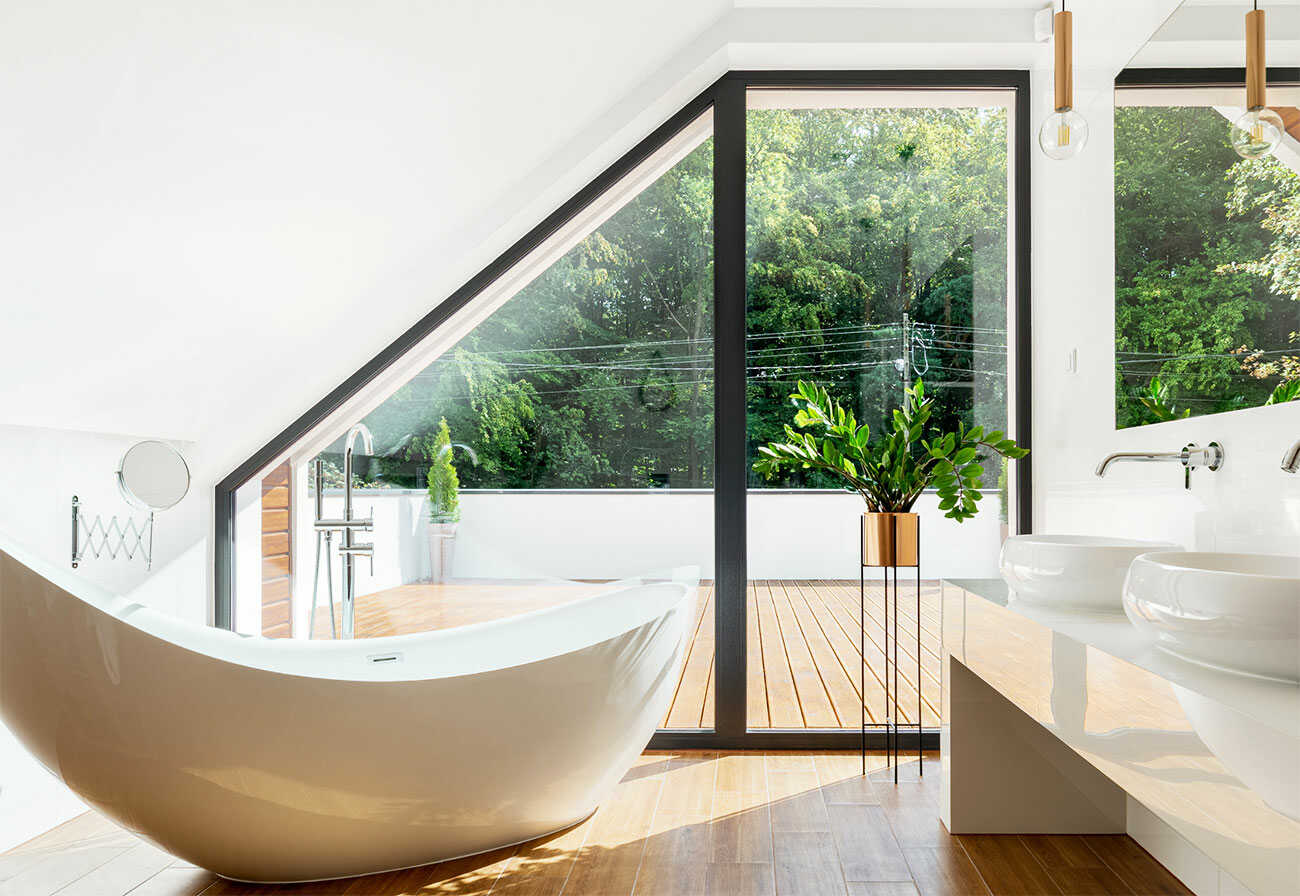 Modern upstairs bathroom with a bathtub facing a large window overlooking a deck.