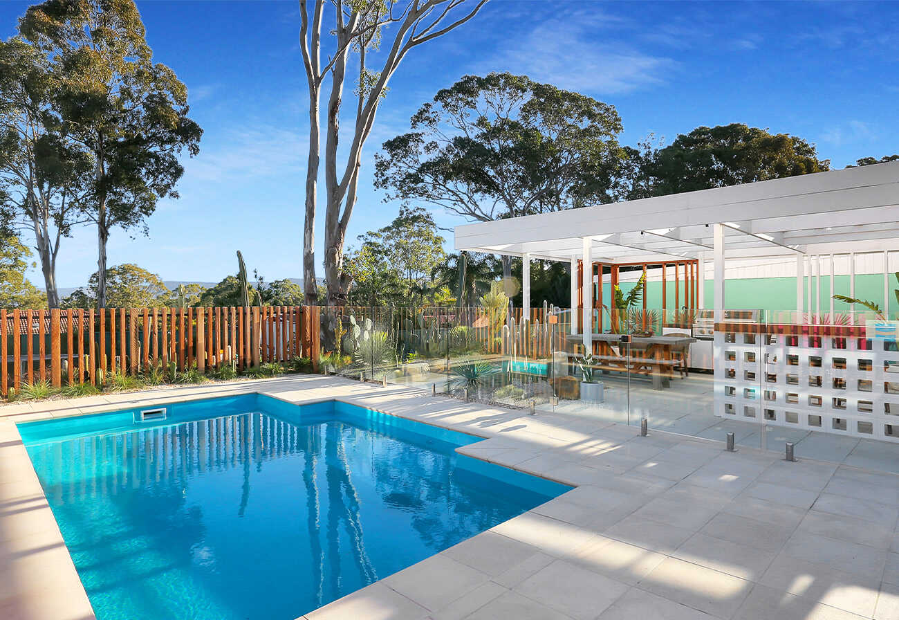 Residential pool area with white stone pavers and a glass fence.