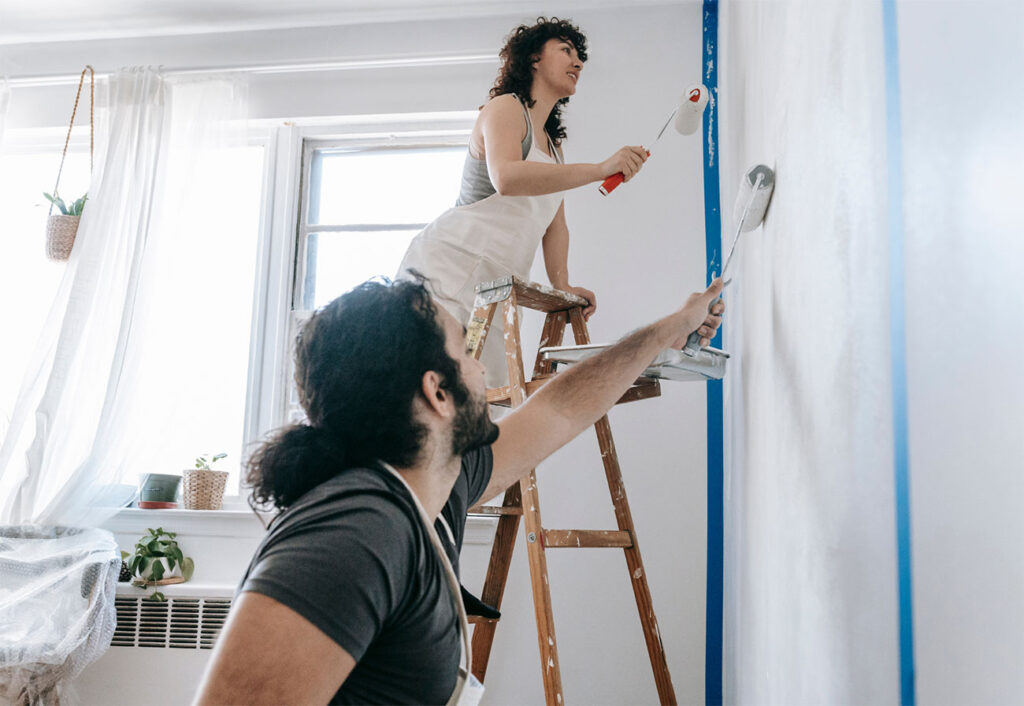 Couple painting a white with white paint and rollers.