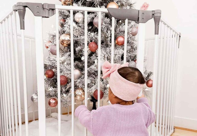 Baby looking through a white playpen at a christmas tree.