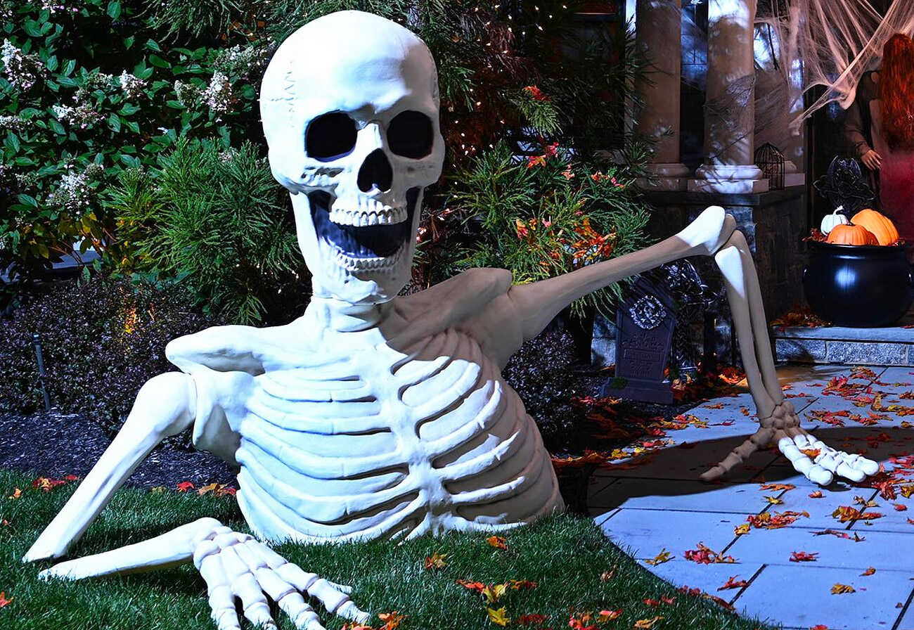 Huge skeleton prop for Halloween positioned on a front lawn.