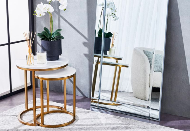 Set of nesting tables with white marble tops and gold rims next to a large mirror.