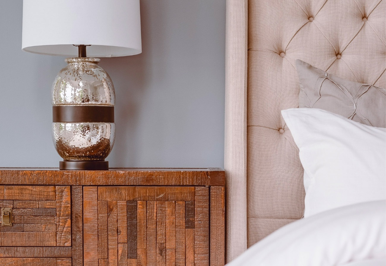 A wooden bedside table with a lamp on top of it.