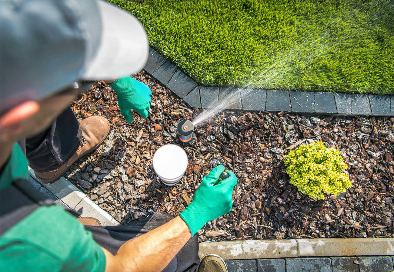 Man tending to an irrigation system on a backyard lawn.