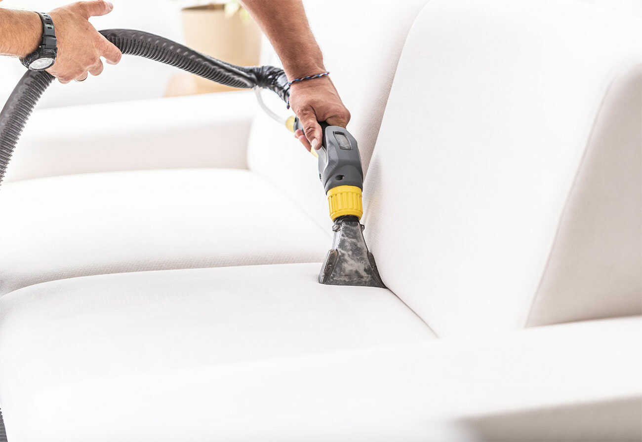 Person vacuuming a white sofa.