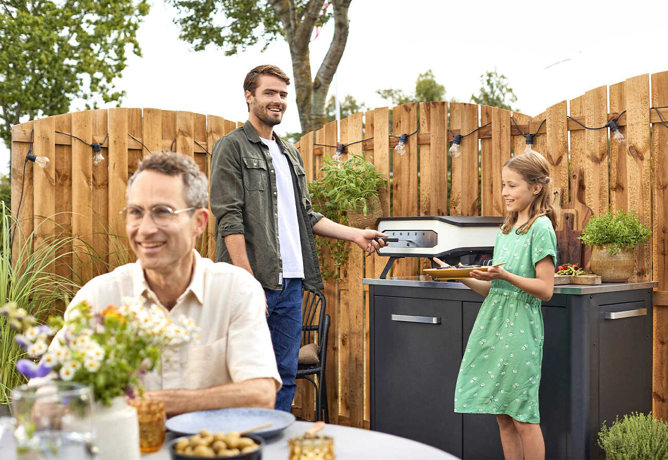 A family making and enjoying pizza outdoors.