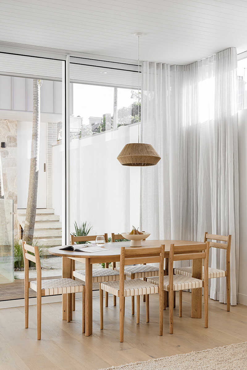 Dining room with oval wooden table and sheer curtains.