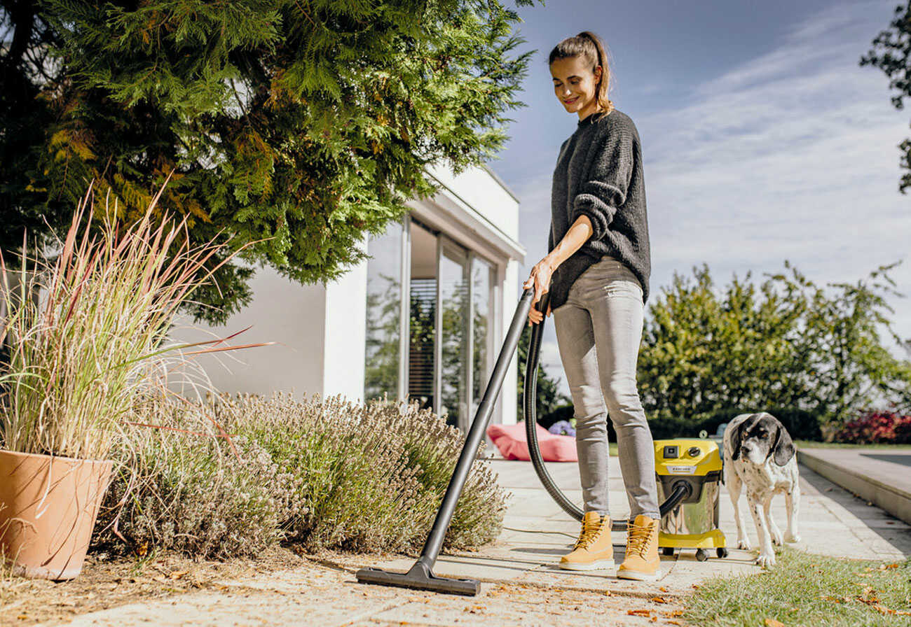 Woman vacuums plant debris on a foothpath.