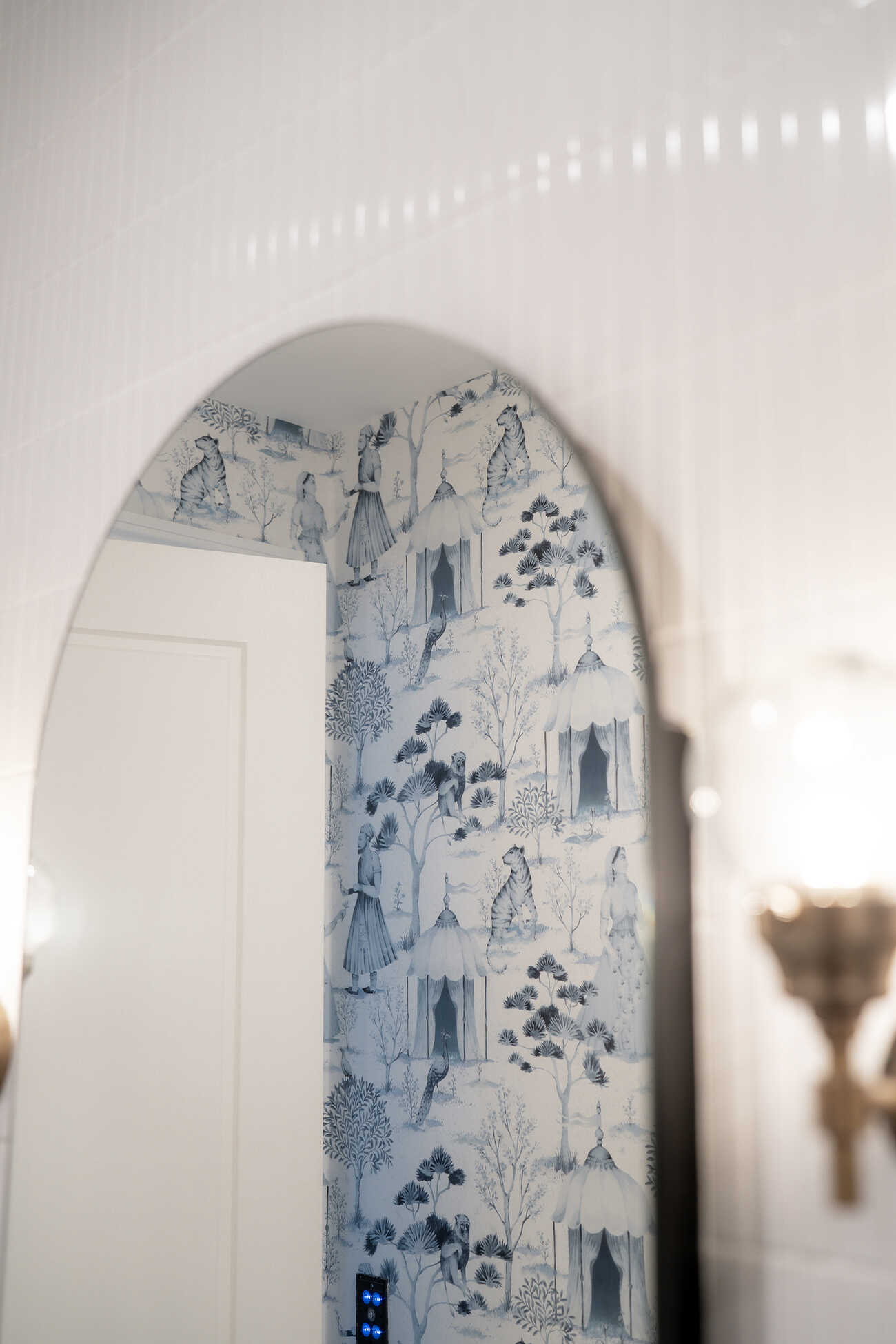 Arched bathroom mirror reflecting blue wallpaper on opposite wall.