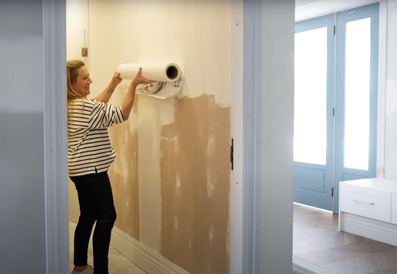 Nikki hanging a roll of wallpaper against a bathroom wall.