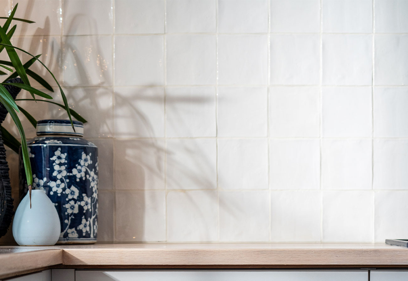 Gloss square laundry splashback tiles above an oak bench. 