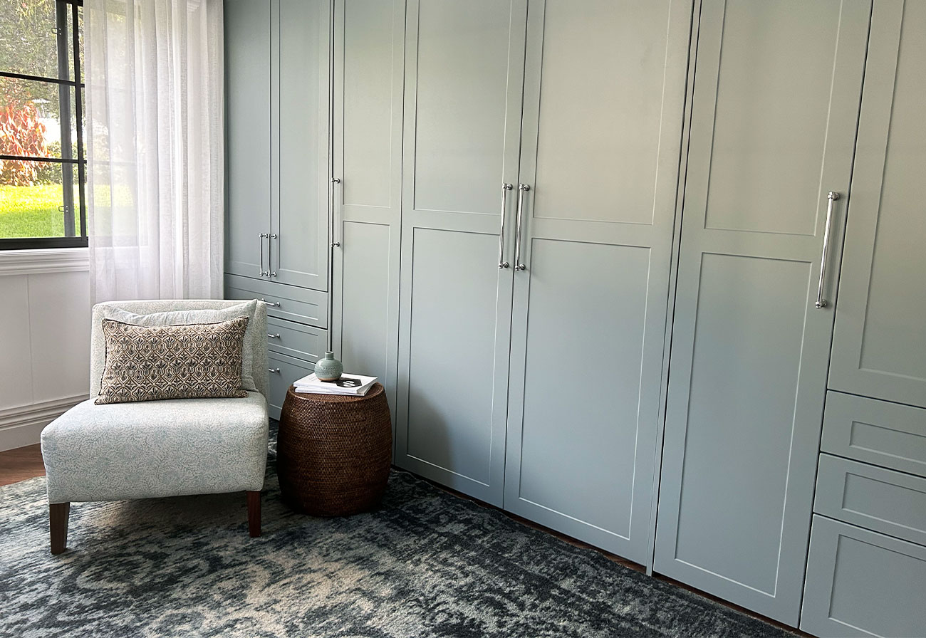 Study with sage cabinetry and a white accent chair.