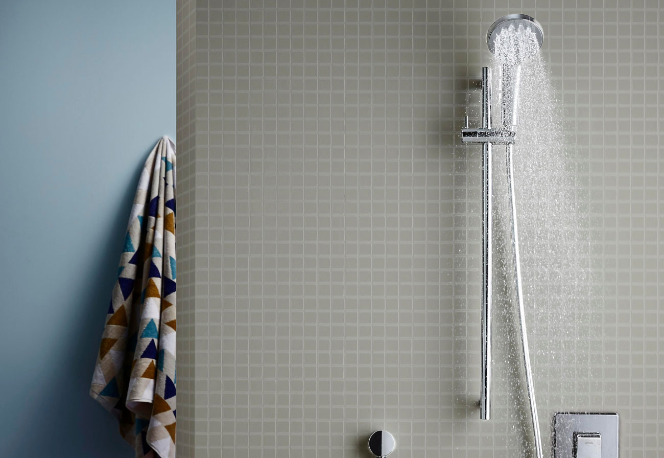 Grey tiles shower cubicle with Methven shower head turned on.