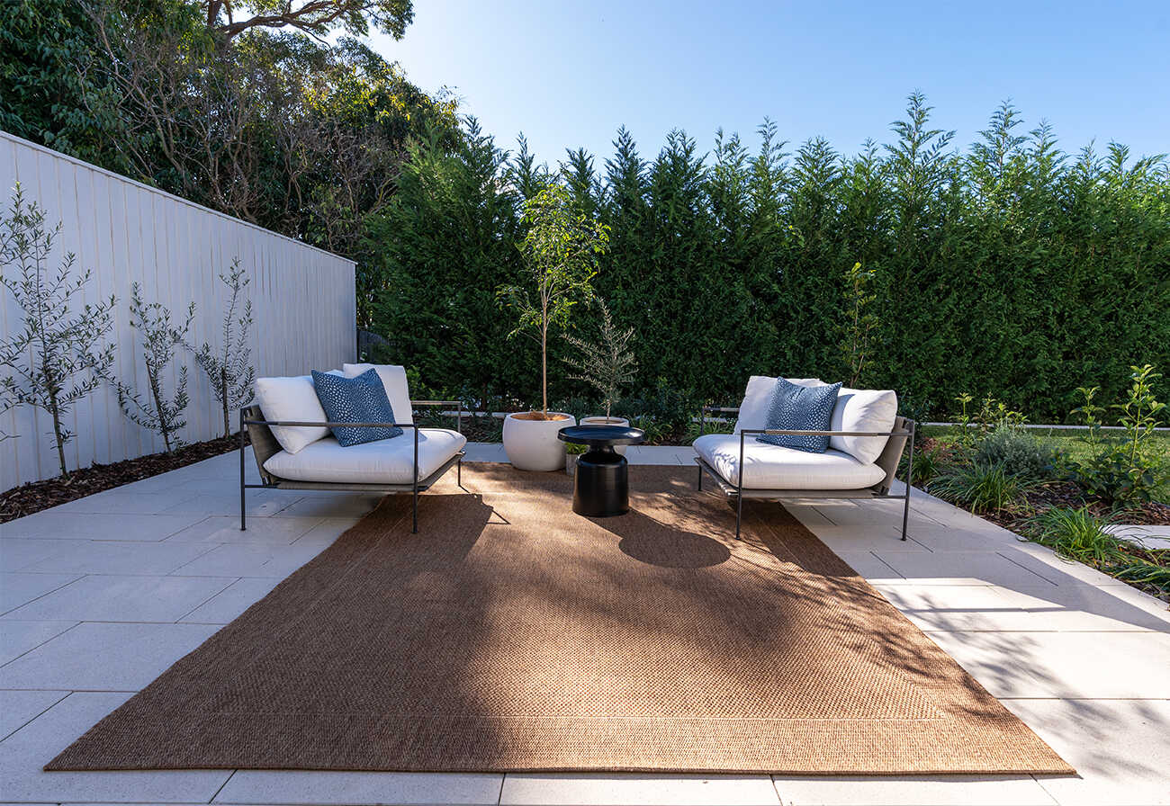 Outdoor patio with white pavers, rug and armchairs.