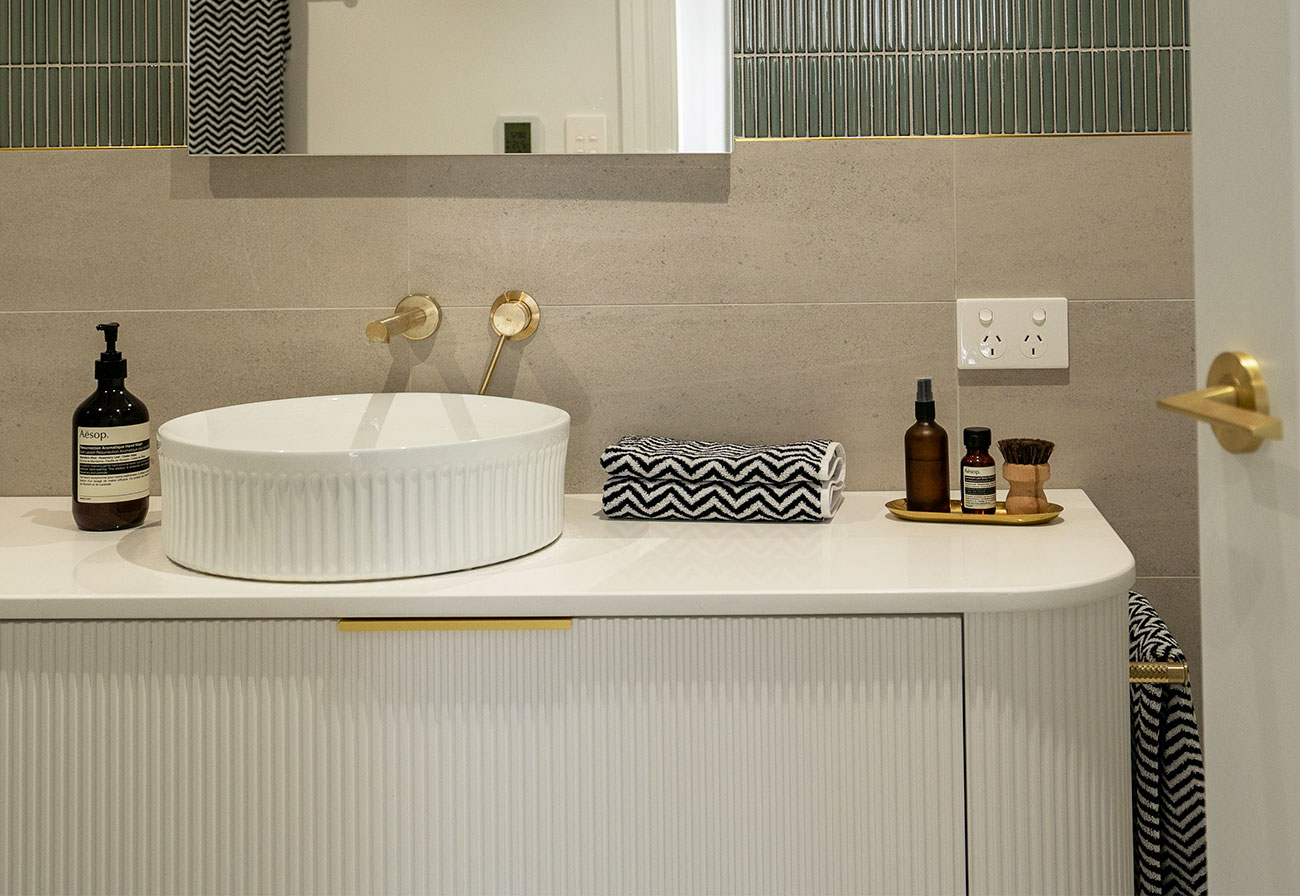 White bathroom with brushed brass tapware and round basin.