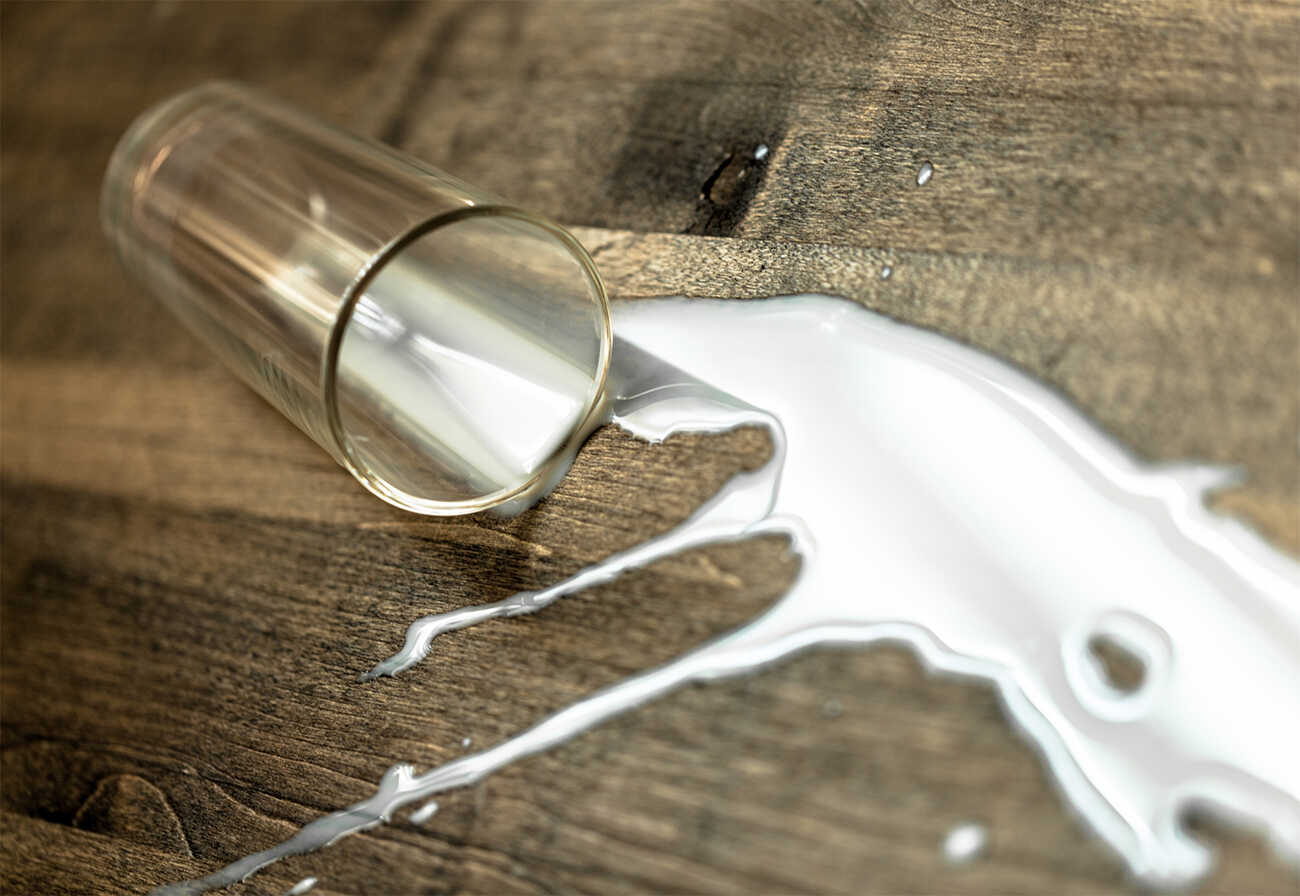 Spilled glass of milk on a wooden floor.