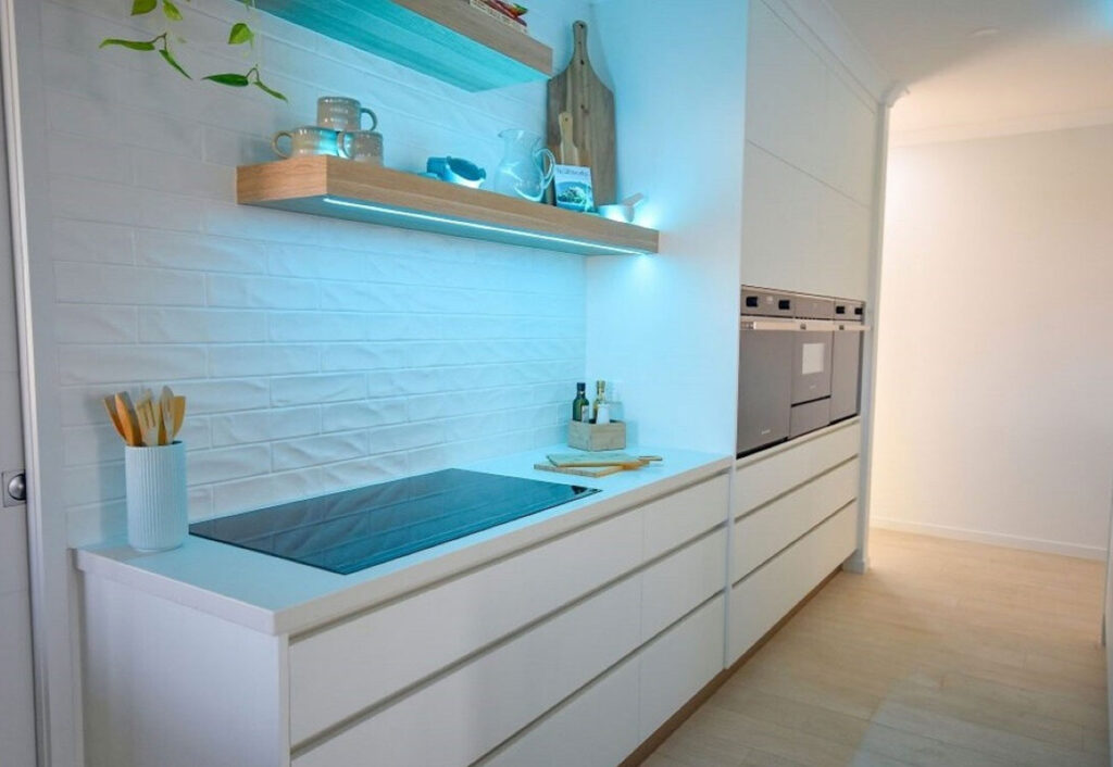 White kitchen with bagged brick splashback and exposed timber shelves.