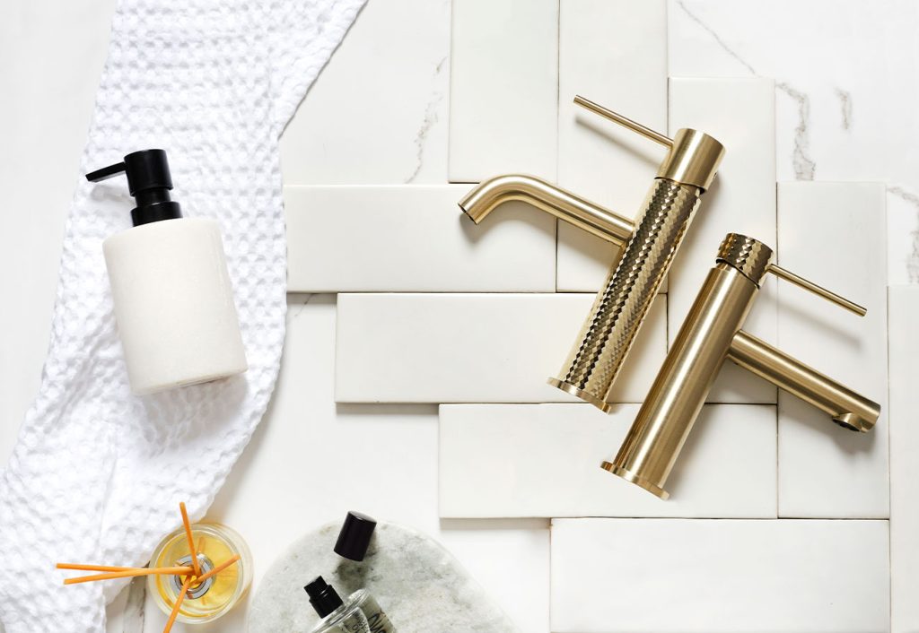 Greens brushed brass mixer taps on assorted tiles.