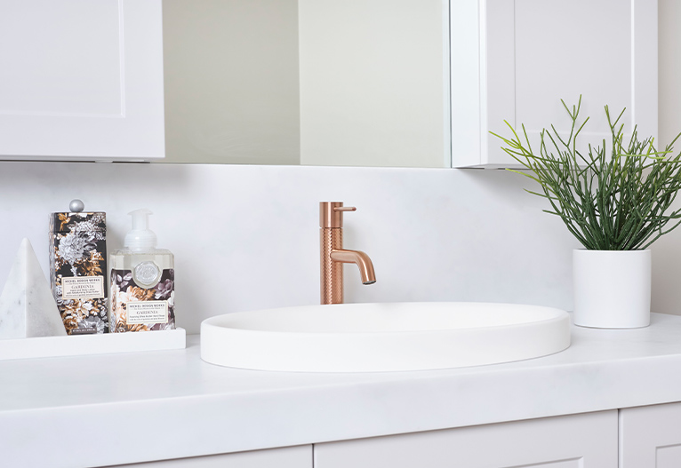 White vanity with small plant and brushed copper tap.