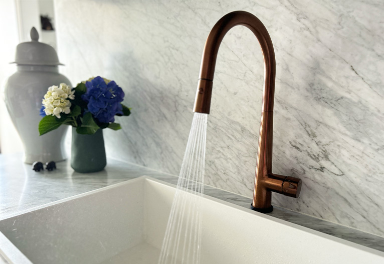 Copper kitchen tap running to a  large white sink.