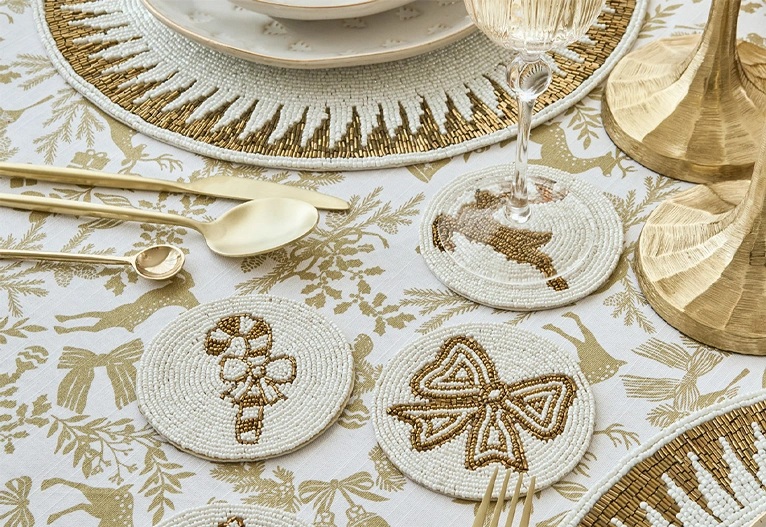 Christmas beaded coasters on a table with gold tableware. 