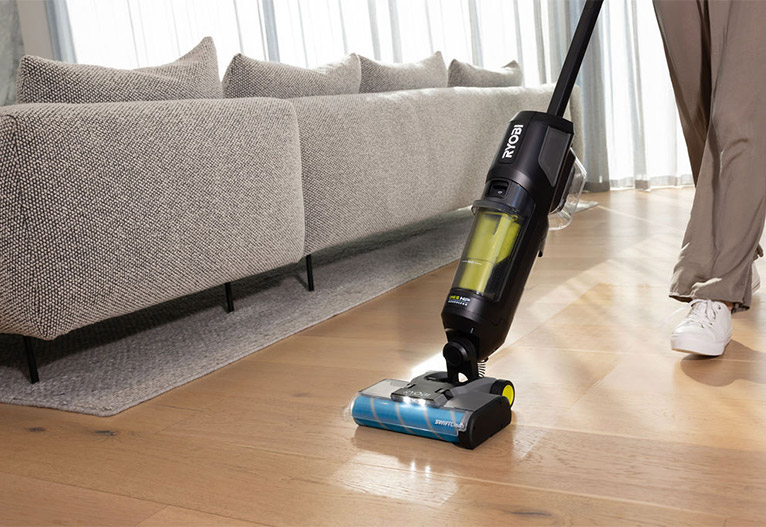 Person vacuuming behind a sofa.