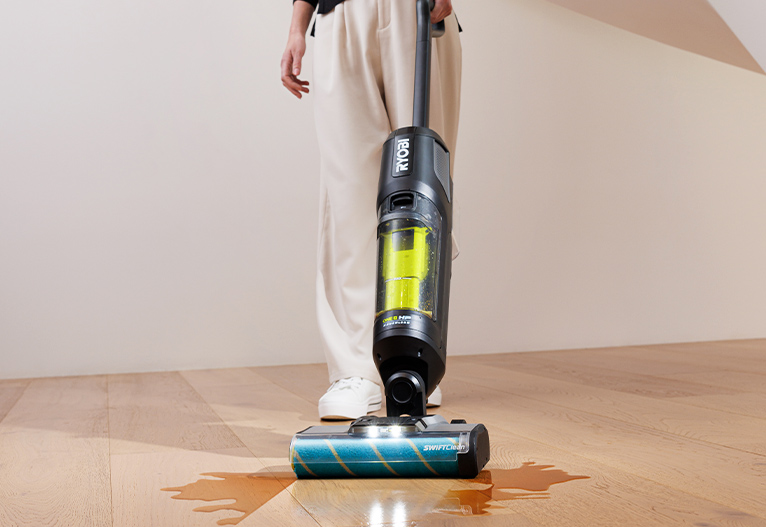 Person using the RYOBI 18V Wet and Dry Hard Floor Cleaner on wet floorboards.