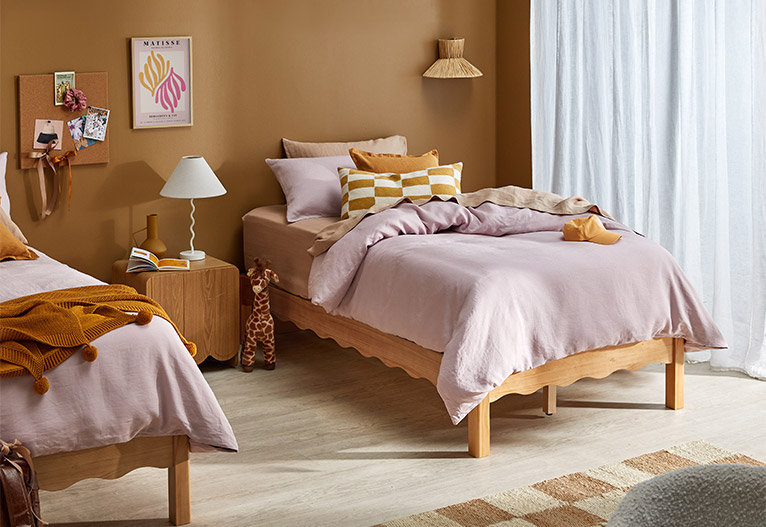 Wooden single beds with scalloped edges dressed with pink quilt covers.