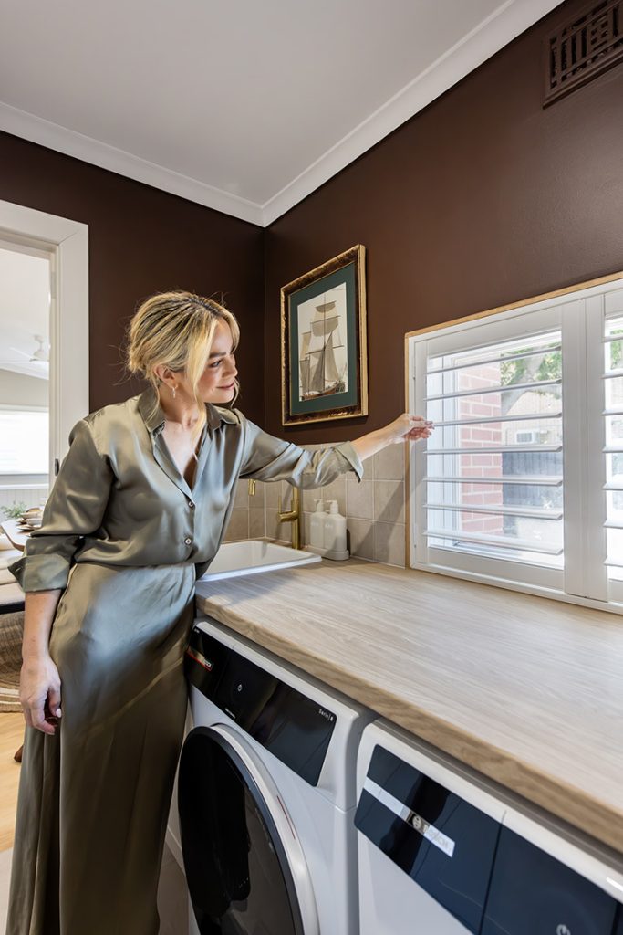 Woman opening launder blinds above a benchtop.