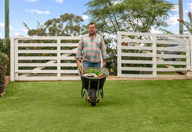 Jason Hodges pushing a wheelbarrow across turf.