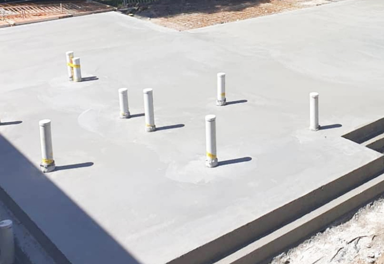 Freshly prepared concrete slab with plumbing pipes exposed.