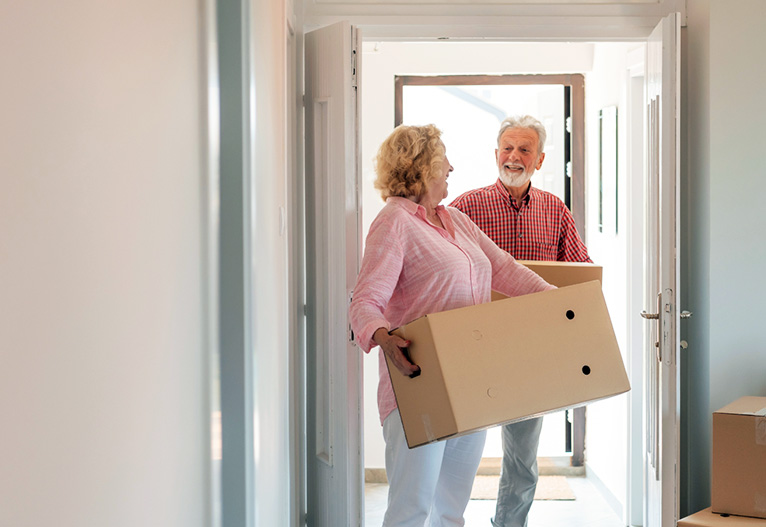 Older couple carrying moving boxes.