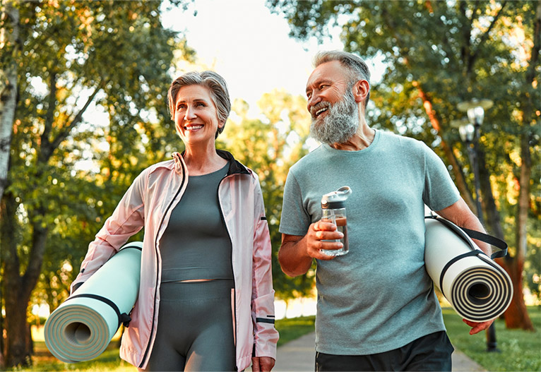 Older healthy couple walking with yoga mats.