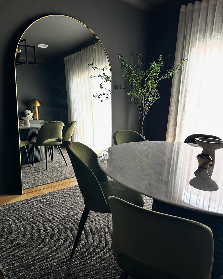 Colour-drenched dining room in dark grey with a large arched floor mirror.