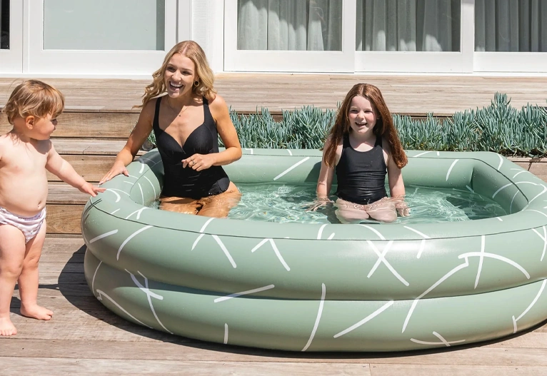 A woman and two children playing in a paddling pool on a deck.