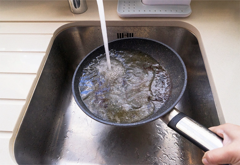 Greasy pan being rinsed in a kitchen sink.
